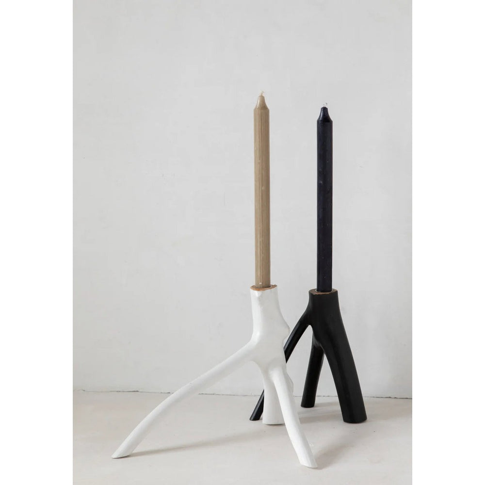Two candle holders, one white and one black, with candles inside on a light background.
