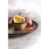 Halved passion fruit in a small bronze bowl on a marble surface
