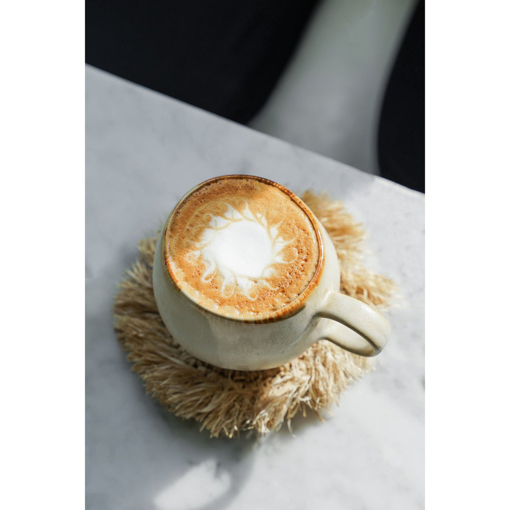 White ceramic mug with a latte on a textured coaster on a marble surface